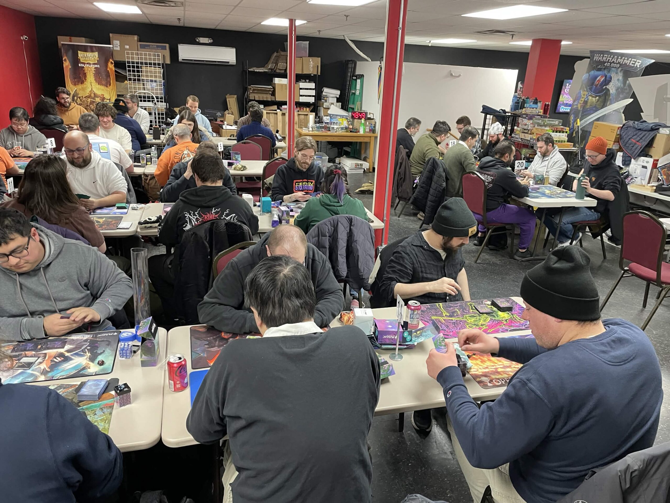 A lively tabletop gaming event with participants focused on their games at multiple tables in a vibrant community setting